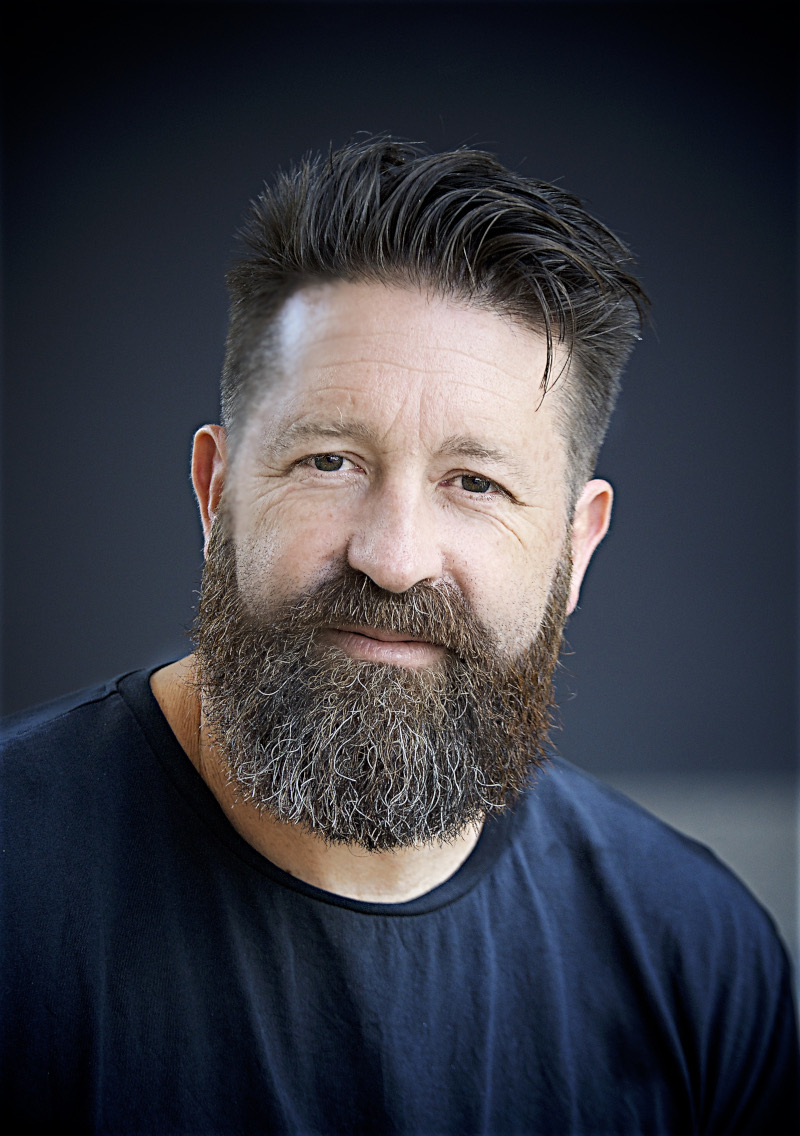 Nigel Poulton wearing a large beard and blue t-shirt with dark blue background